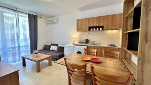 A compact living space with a kitchenette, a dining area with wooden furniture, a sofa, and a washing machine.