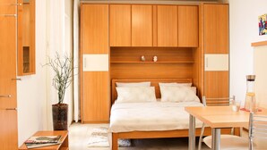 Un dormitorio con cama de madera, una mesita de noche, una silla, una pequeña mesa y una planta en maceta.