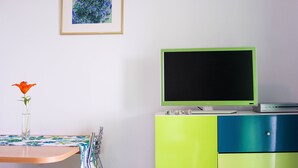 Una habitación con una televisión sobre un mueble, un cuadro en la pared y un florero con una flor sobre una mesa.