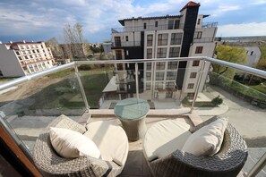 Un balcon doté de meubles en osier et d’une rambarde en verre, donnant sur un quartier résidentiel.