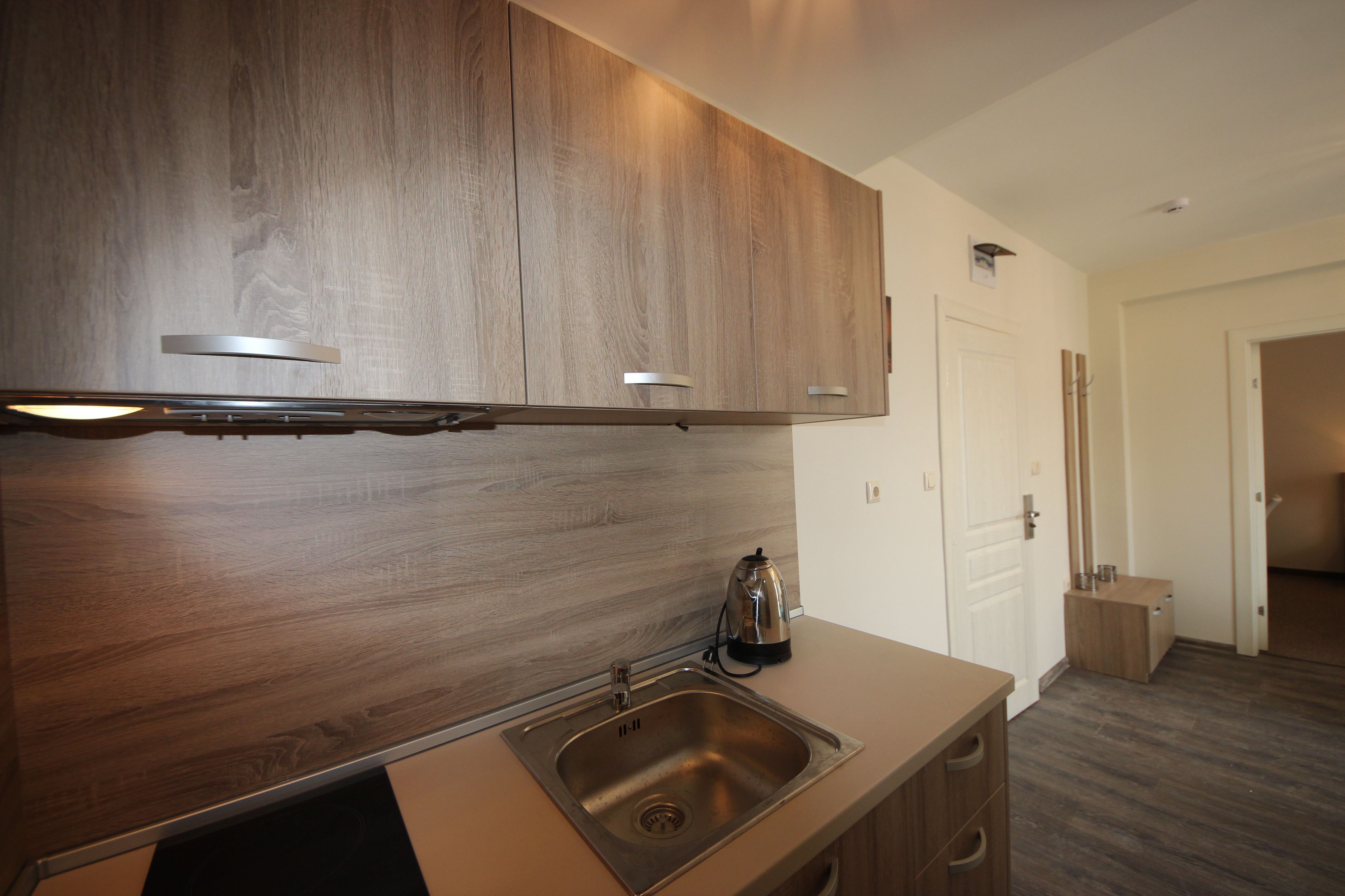 A modern kitchen with wooden cabinets, a stainless steel sink, and a kettle.