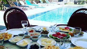 A table set for a meal with various dishes, including bread, olives, and vegetables, by a poolside.