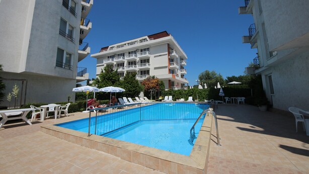 A swimming pool with lounge chairs and umbrellas, surrounded by buildings with balconies and a clear sky. - Menada Apartments in Azzuro Hotel (Sunny Beach)