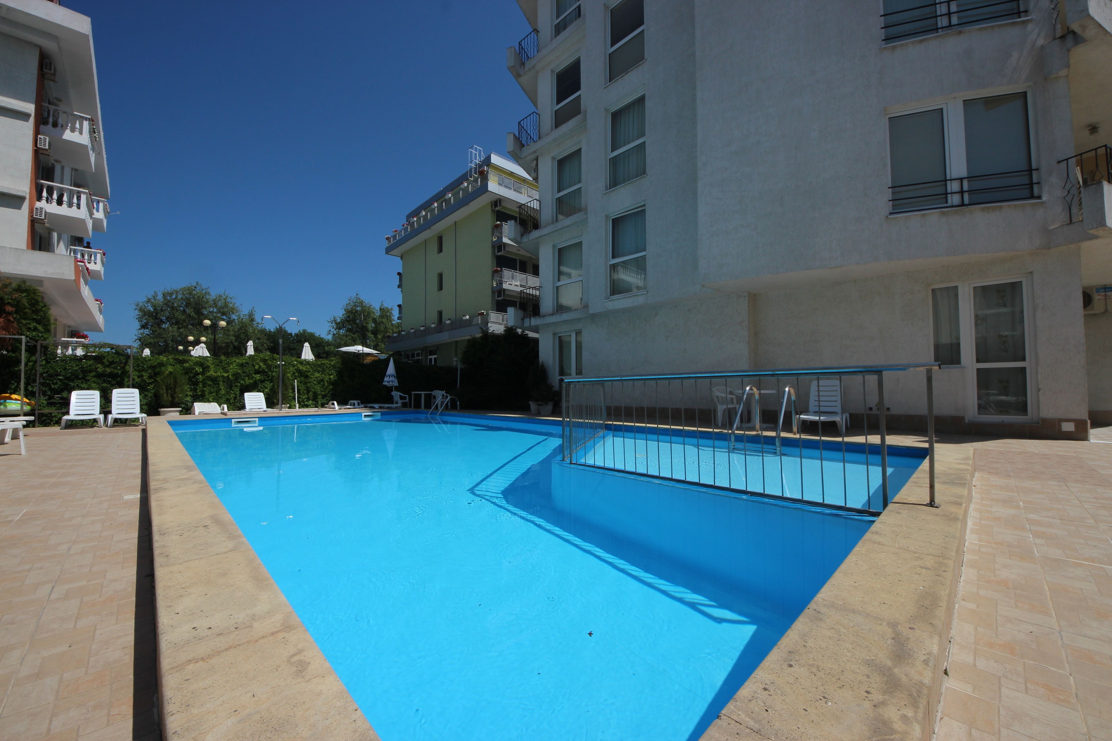 A swimming pool with a tiled deck, surrounded by white buildings with balconies.