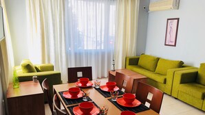 A dining area with a wooden table set for four, red bowls and plates, and a green sofa in the background. - Menada Apartments in Azzuro Hotel (Sunny Beach)