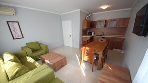 A compact living space with a green sofa set, a wooden dining table, and a kitchenette with wooden cabinets and a microwave. - Menada Apartments in Azzuro Hotel (Sunny Beach)