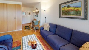 Un salón con sofá azul, suelo de madera, zona de comedor con mesa y sillas, y un cuadro enmarcado en la pared.
