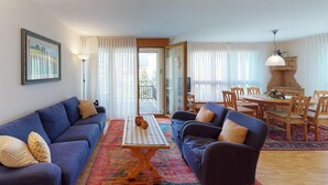 Una sala de estar con un sofá azul, un sofá más pequeño, una mesa de centro y un comedor con una mesa y sillas de madera.
