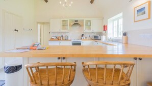 A kitchen with wooden chairs, a central island, and white cabinets. - Pigsty Cottage - Luxurious apartment within orangery (Melksham)