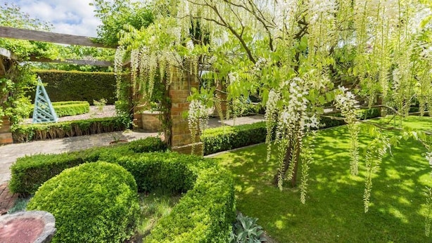 A well-maintained garden with neatly trimmed hedges, a variety of flowering trees, and a brick wall. - Pigsty Cottage - Luxurious apartment within orangery (Melksham)