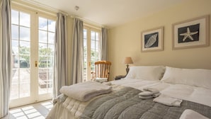 A hotel room with a large bed, a wooden chair, a nightstand, and a view through the glass doors. - Pigsty Cottage - Luxurious apartment within orangery (Melksham)