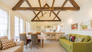 A spacious living area with a high ceiling, a dining table with chairs, a sofa, and a kitchen in the background. - Pigsty Cottage - Luxurious apartment within orangery (Melksham)