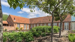 A brick building with a red-tiled roof, surrounded by a garden with various plants and trees. - Pigsty Cottage - Luxurious apartment within orangery (Melksham)