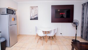 A modern kitchen with a microwave, refrigerator, and dining table with chairs. - Prestigious Apartments (Randburg)