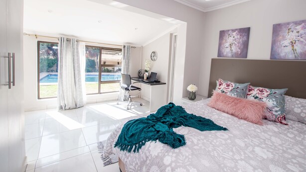 A bedroom with a large bed, a desk, and a view of a swimming pool. - Prestigious Apartments (Randburg)