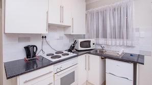 A compact kitchen with white cabinets, a microwave, a kettle, and a sink. - Prestigious Apartments (Randburg)