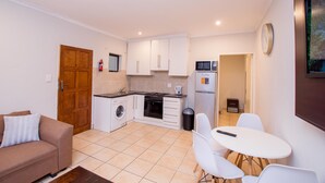A compact kitchen with white cabinets, a microwave, and a stove. There is a dining area with a table and chairs, and a sofa in the living area. - Prestigious Apartments (Randburg)