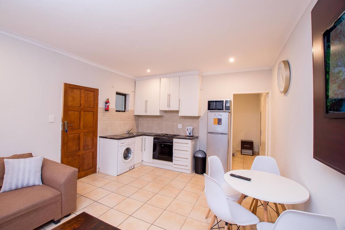A compact kitchen with white cabinets, a microwave, and a stove. There is a dining area with a table and chairs, and a sofa in the living area.