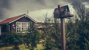 A wooden house with a red roof, surrounded by dense greenery and a cloudy sky. - Hekla Holiday Home (Storinupur)