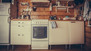 A compact kitchen with a white stove, oven, and refrigerator. There are wooden cabinets and a wooden wall. - Hekla Holiday Home (Storinupur)