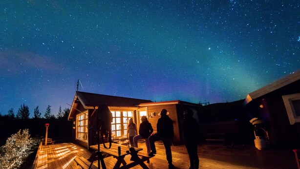A wooden deck with people gathered around a table, under a starry night sky. - Hekla Holiday Home (Storinupur)