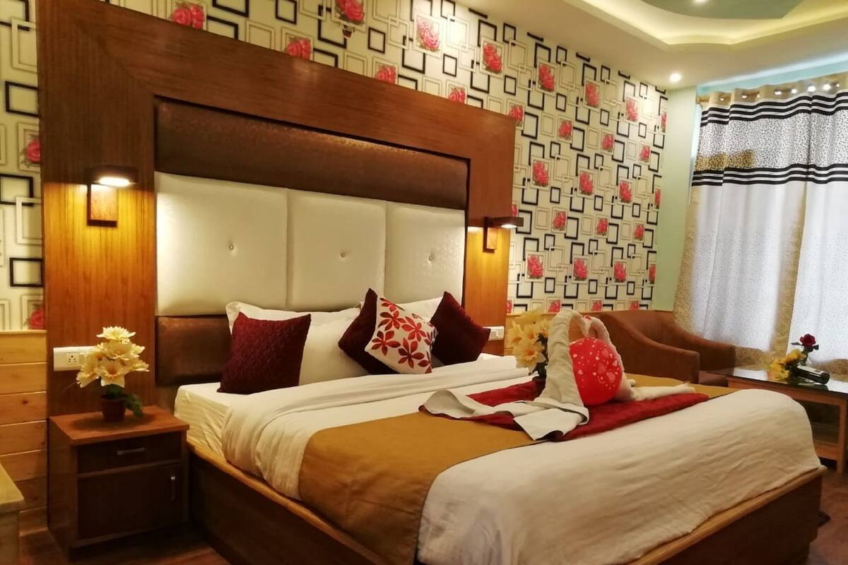 A neatly made bed with a wooden headboard, a nightstand with a vase of flowers, and a patterned wall in the background.