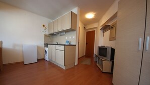 A compact kitchen with a washing machine, a small refrigerator, and a television on a stand. - Menada Apartments in Rainbow 1 Complex (Sunny Beach)