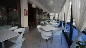 A restaurant interior with white tables and chairs, large windows with curtains, and hanging pendant lights. - Menada Apartments in Rainbow 1 Complex (Sunny Beach)