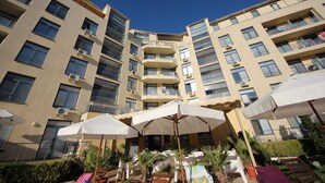 A multi-story hotel with balconies, outdoor umbrellas, and potted plants. - Menada Apartments in Rainbow 1 Complex (Sunny Beach)