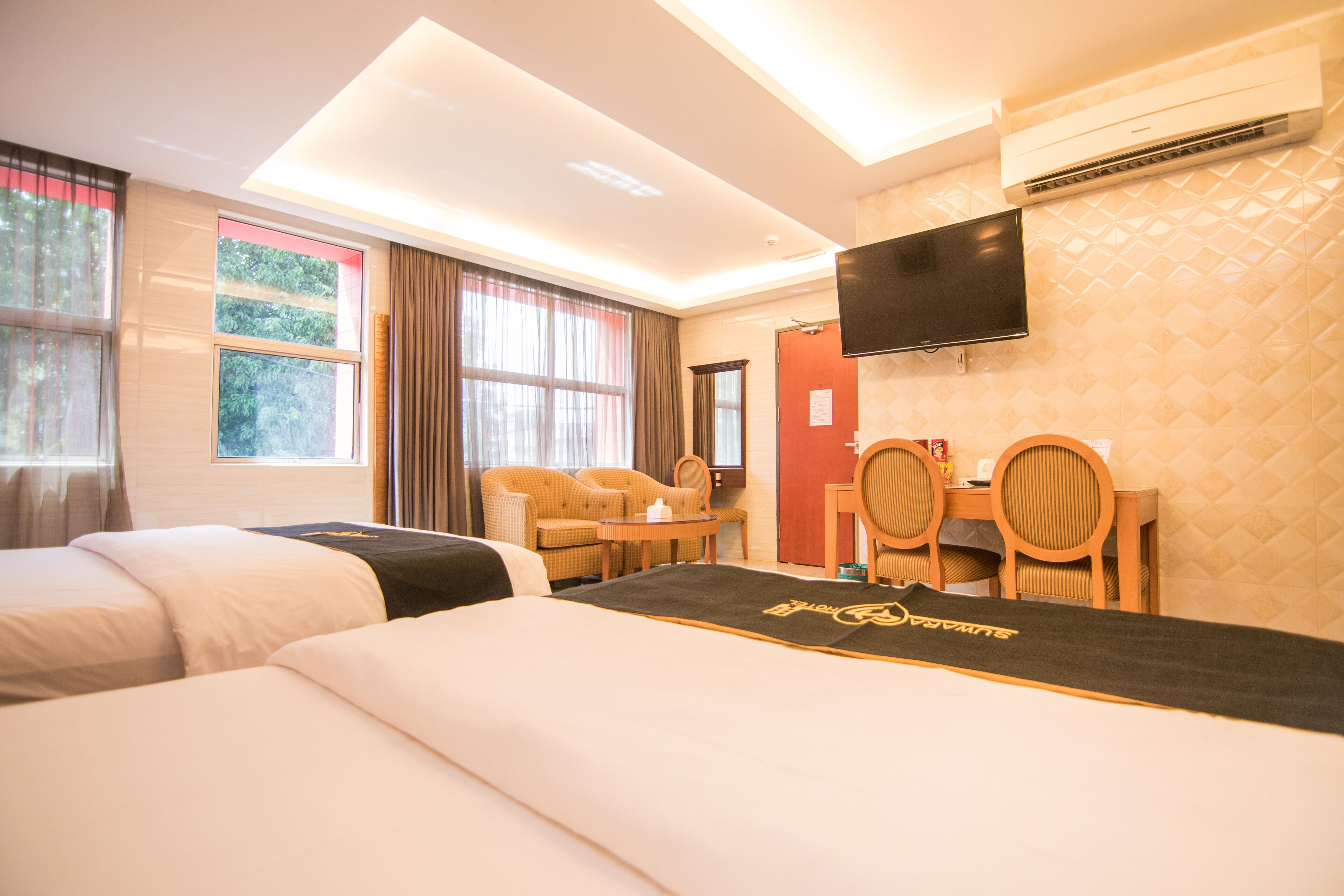 Une chambre d’hôtel avec deux lits, un bureau, des chaises, une télévision et un appareil de climatisation.