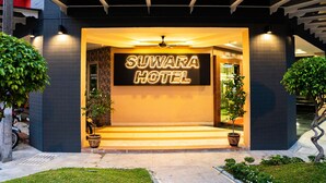 El exterior del Hotel Suwara, con un llamativo letrero iluminado, una entrada techada y plantas en macetas.