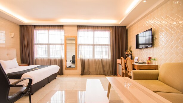Habitación de hotel con cama, escritorio, sofá, televisor montado en la pared y ventanas grandes con cortinas.