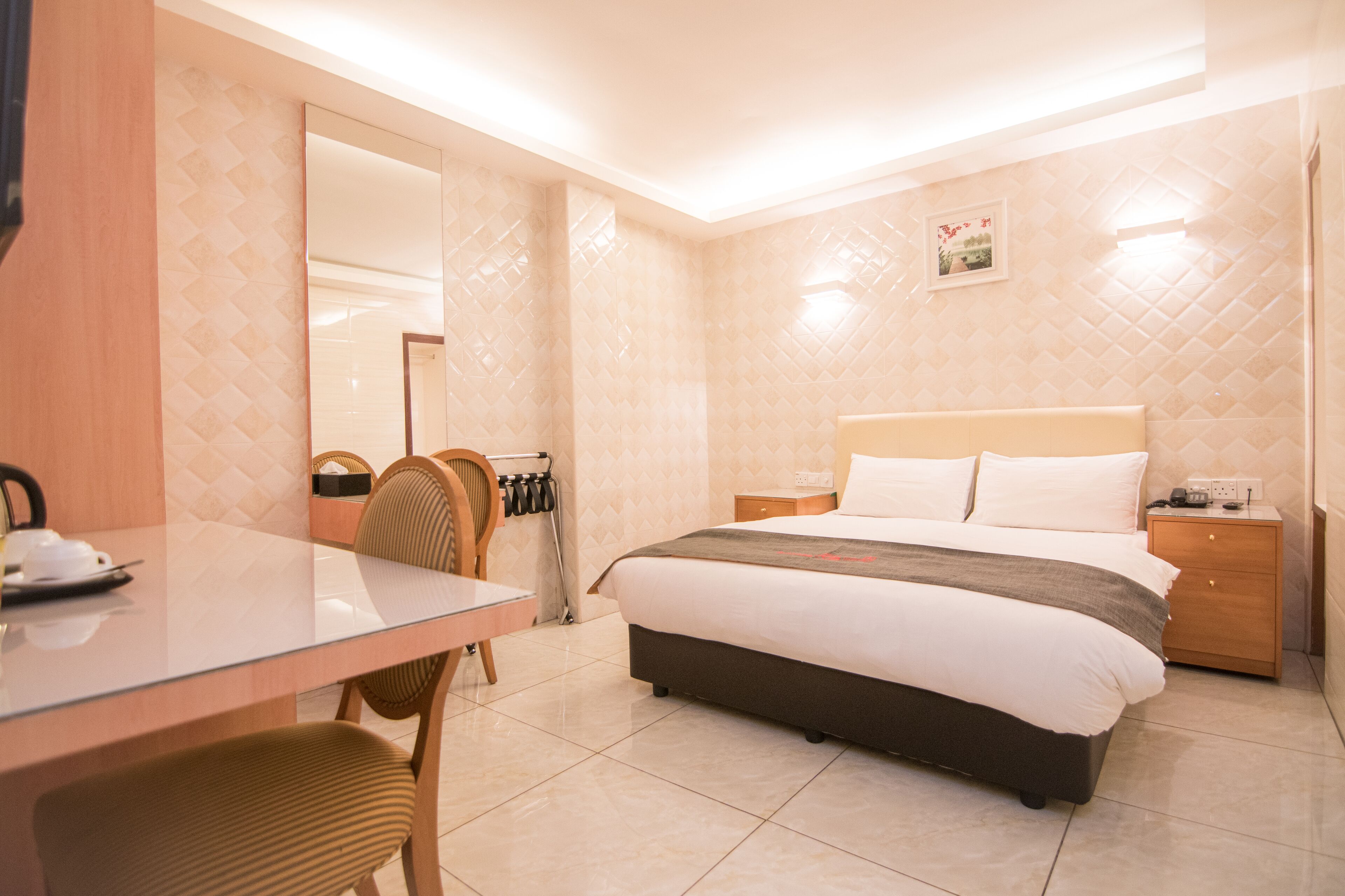 A hotel room with a bed, bedside table, chair, and a small table with a cup and saucer.