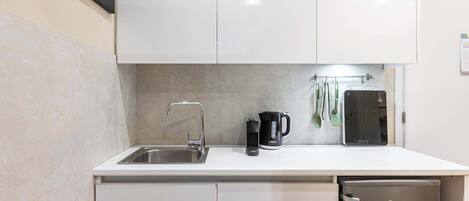 A compact kitchen with a sink, a coffee maker, and a compact refrigerator.