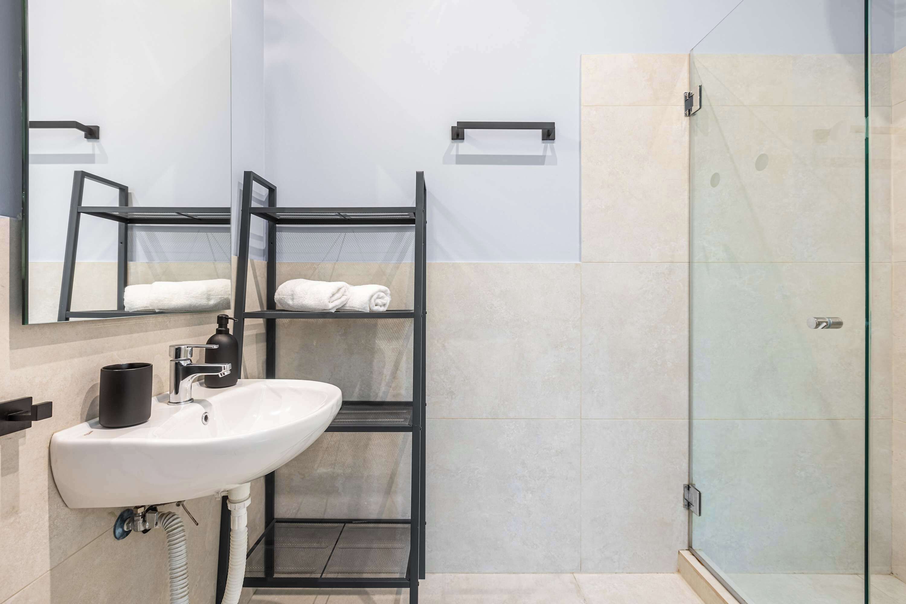 A bathroom with a white sink, a mirror, a towel rack, and a glass shower enclosure.