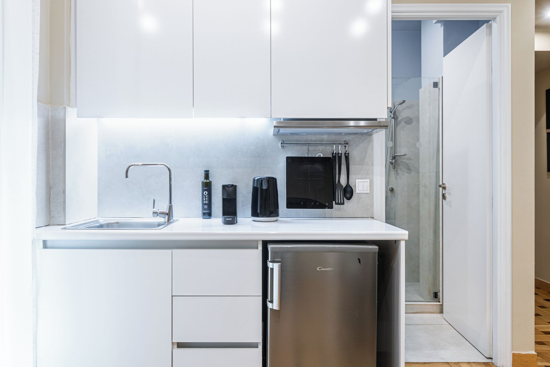 Una cocina moderna con armarios blancos, un refrigerador de acero inoxidable, una tetera, una cafetera y un tostador.