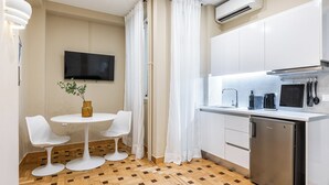Una cucina moderna con mobili bianchi, forno a microonde integrato e lavastoviglie. È presente una piccola zona pranzo con due sedie bianche e un tavolo rotondo.