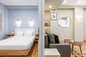 A modern hotel room with a wooden bed, a grey sofa, a small table, and a round mirror. - Kolonaki Suites By Olala Homes (Athens)