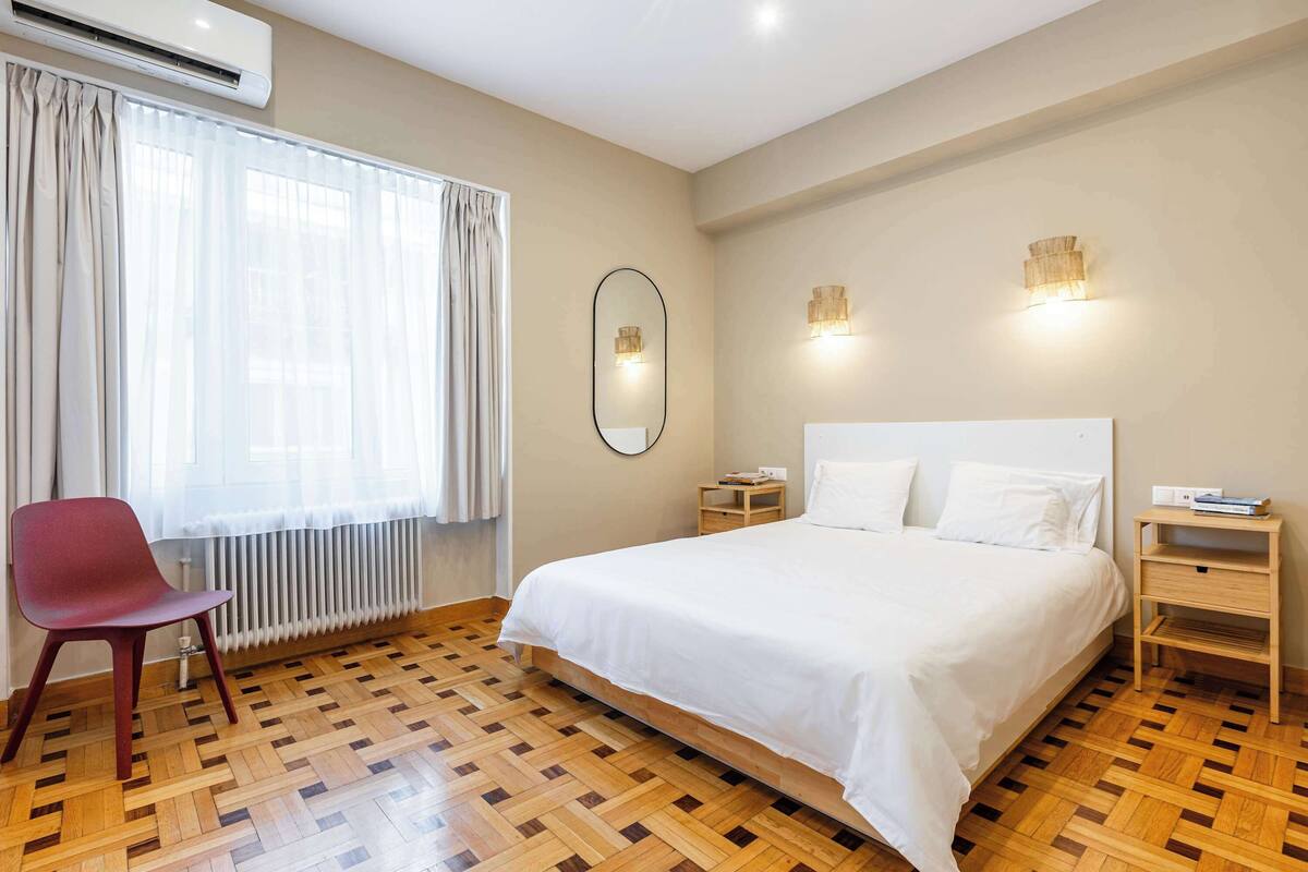 Quarto com uma cama grande, uma cadeira, mesa de cabeceira e um radiador.