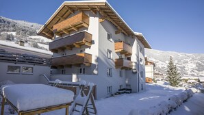 A multi-story building with balconies, a wooden deck, and a snow-covered landscape. - Garni Nill (Schwendau)