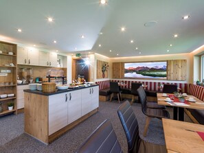 Una cocina moderna con una isla central, zona de buffet, asientos con mesas y sillas, y un amplio ventanal con vistas panorámicas.