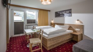 A hotel room with a wooden bed, a desk, and a chair. There is a window with blinds, a lamp, and a painting on the wall. - Garni Nill (Schwendau)