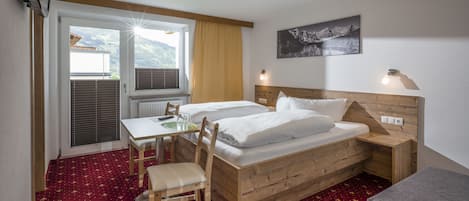 Une chambre d’hôtel avec un lit en bois, un bureau et une chaise. Il y a une fenêtre avec des stores, une lampe et un tableau au mur.