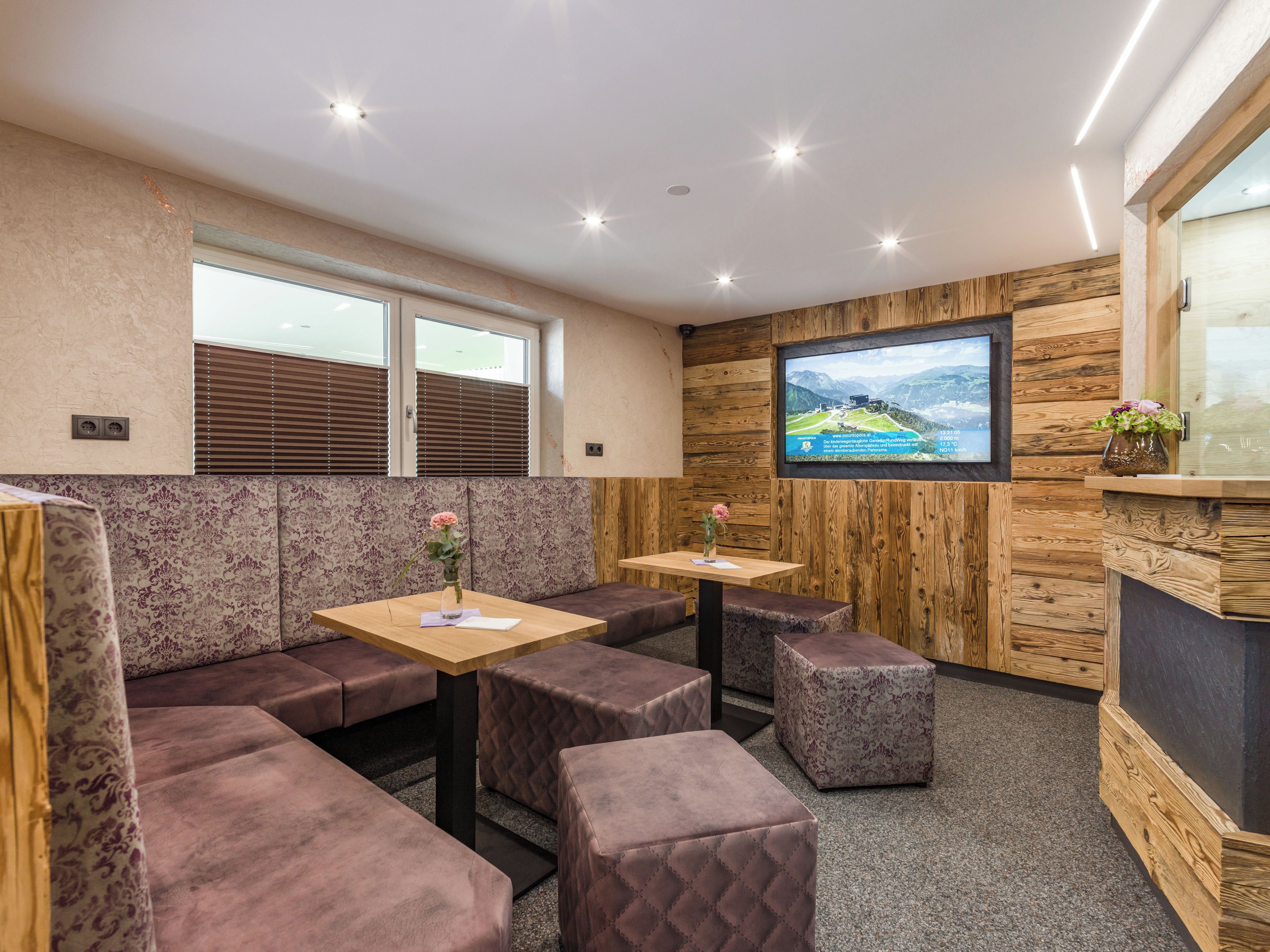 A modern interior with a wooden wall, a flat-screen TV, and a seating area with cushioned benches and ottomans.