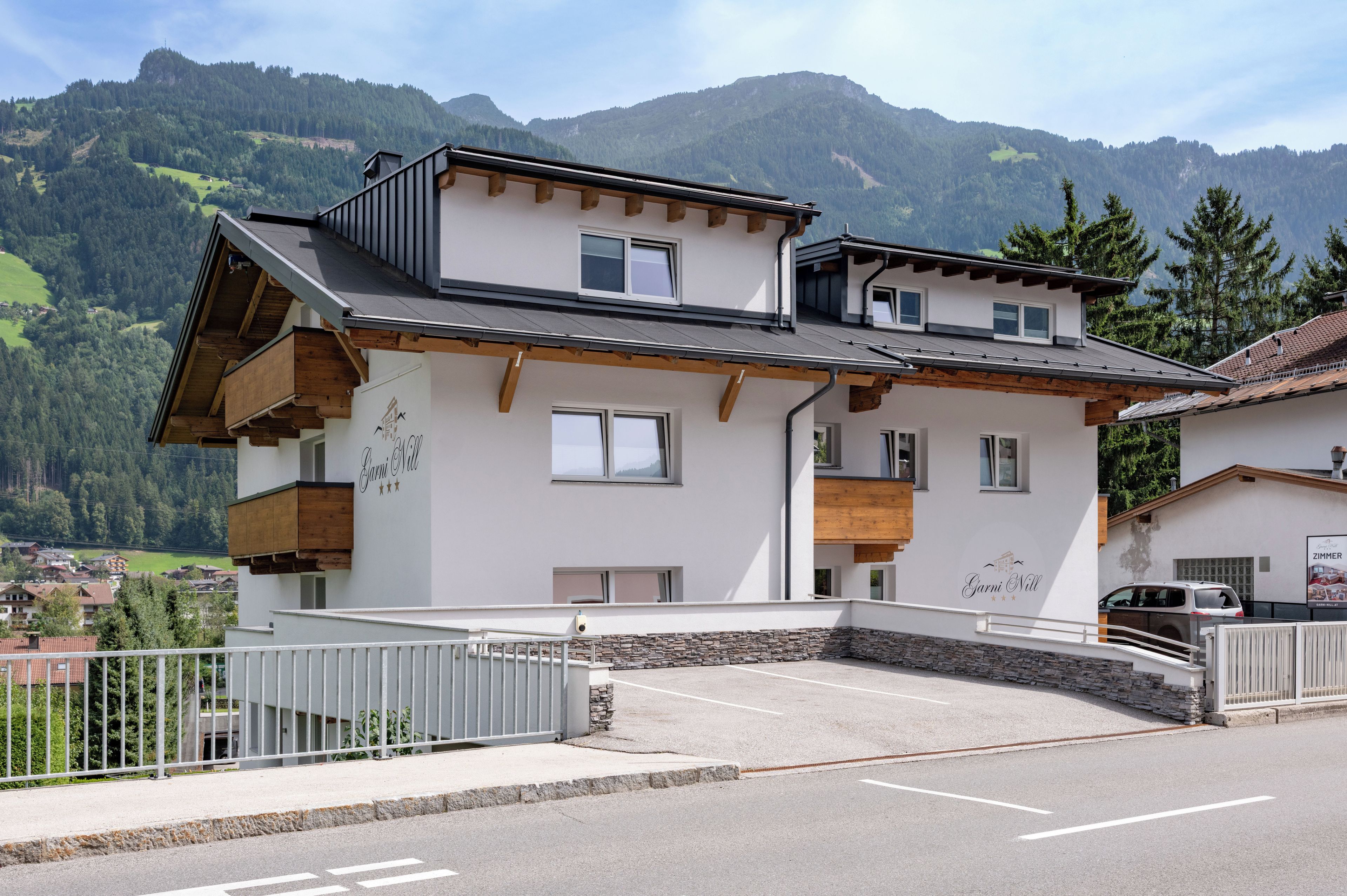 A two-story building with a balcony, a stone facade, and a view of mountains in the background.