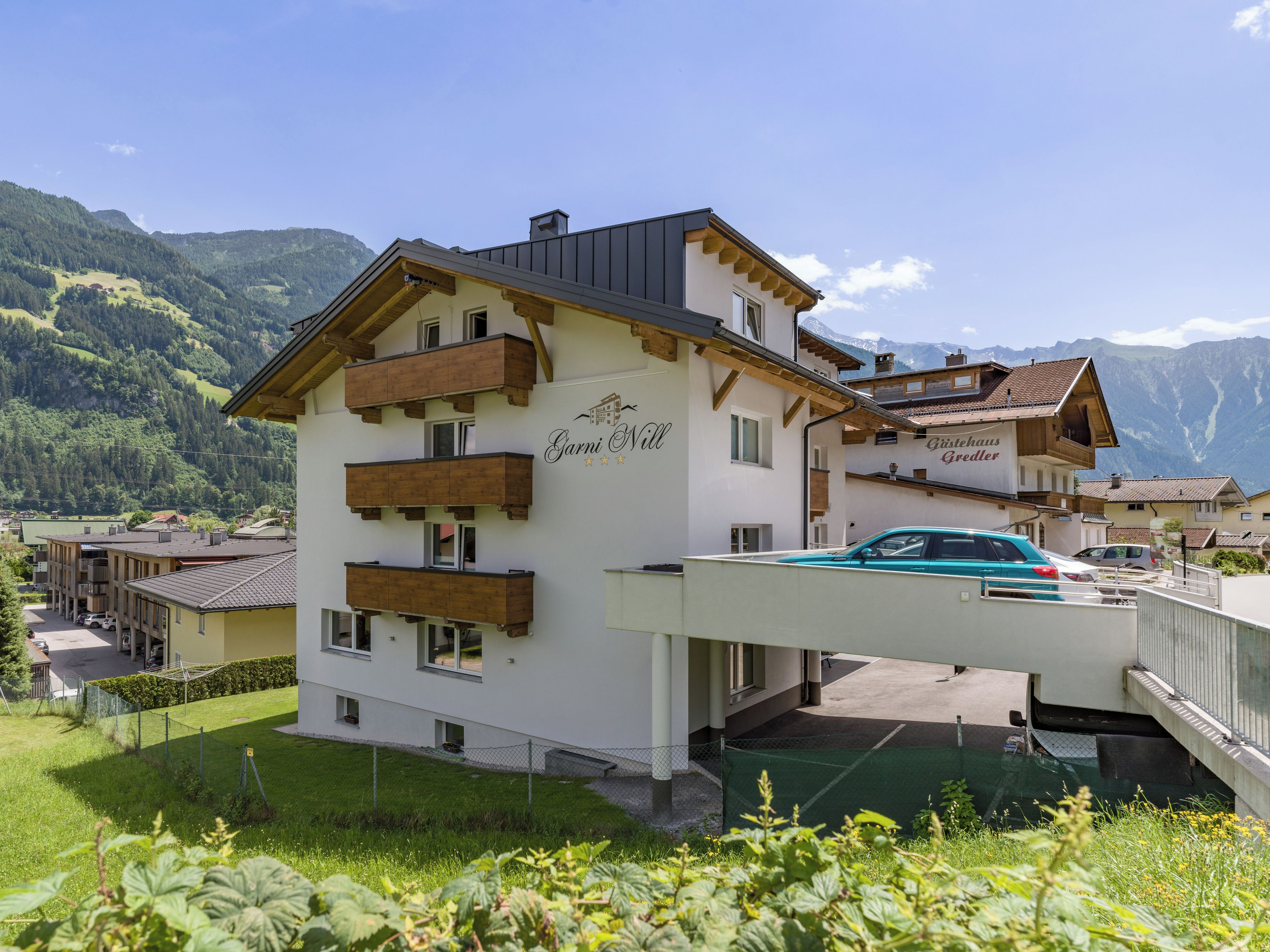 A multi-story hotel with balconies, a covered parking area, and a mountainous backdrop.