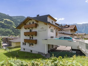 A multi-story hotel with balconies, a covered parking area, and a mountainous backdrop. - Garni Nill (Schwendau)
