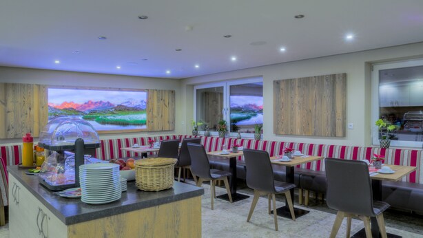 A restaurant with a counter, seating area, and large windows. - Garni Nill (Schwendau)