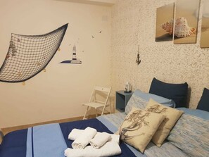 Un dormitorio ordenado con cama, almohadas, un dosel colgante y adornos de pared que incluyen un faro y conchas marinas.
