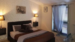 A bedroom with a bed, two bedside lamps, a ceiling fan, a window with curtains, and a wall with a floral pattern. - B&B Fragranza Di Sicilia (Giardini Naxos)